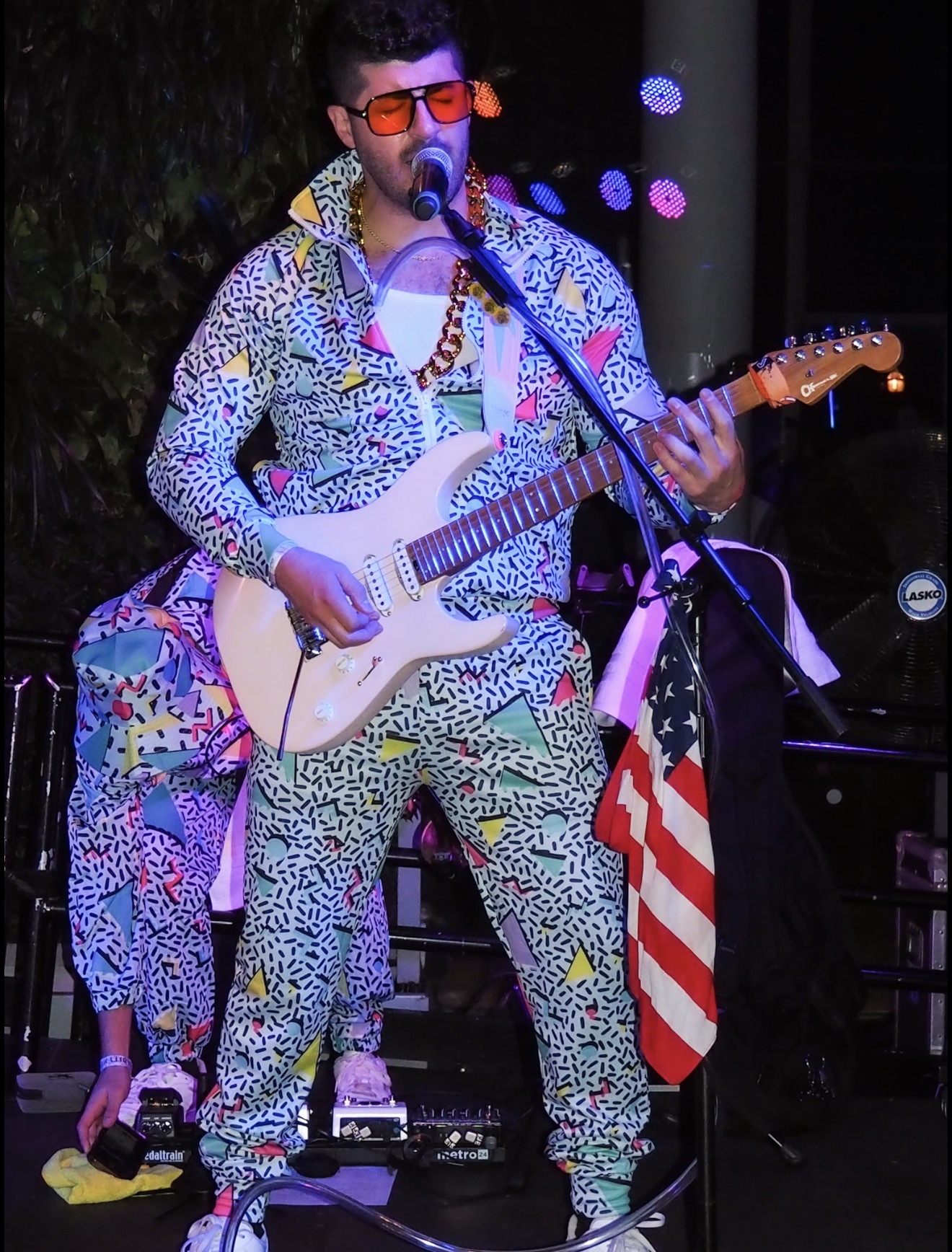 Spotlight frontman in a neon 90s suit singing and playing guitar